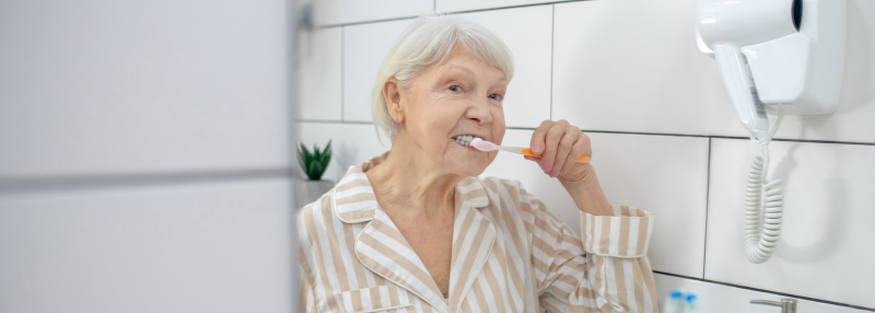 Elderly lady brushing her teeth in the mirror in the bathroom
