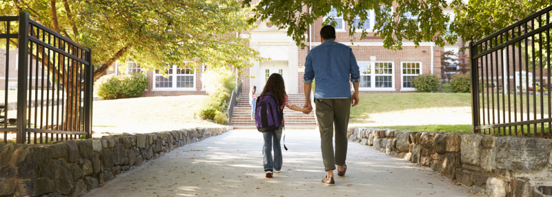 Father and daughter holding hands as they walk up to school