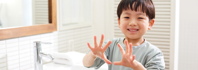 Smiling kid holds up his hands after washing them in the bathroom at home