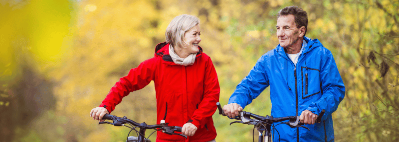 Active older man and woman walking outside by their bikes