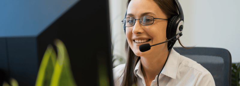 Smiling female customer care representative with black headset on looking at computer
