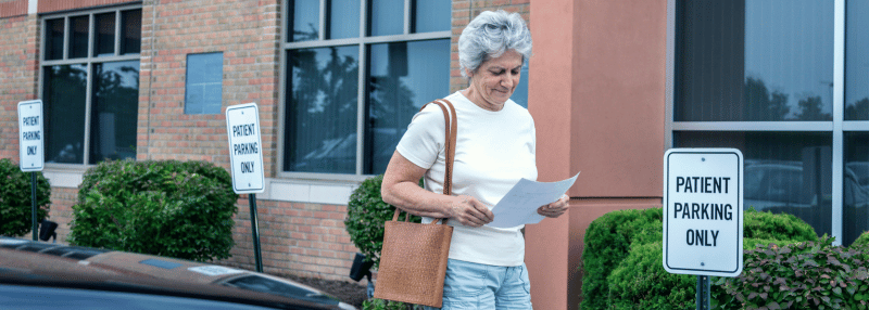 Senior woman leaving doctor's appointment and looking relieved, smiling at the papers in her hand