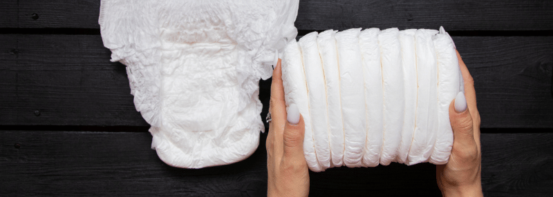 Woman's hands holding stack of adult diapers with adult diaper displayed flat next to it